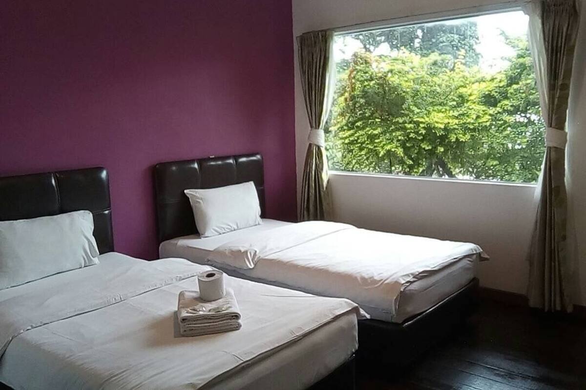 Habitación de hotel con dos camas, paredes moradas y un ventanal con cortinas.