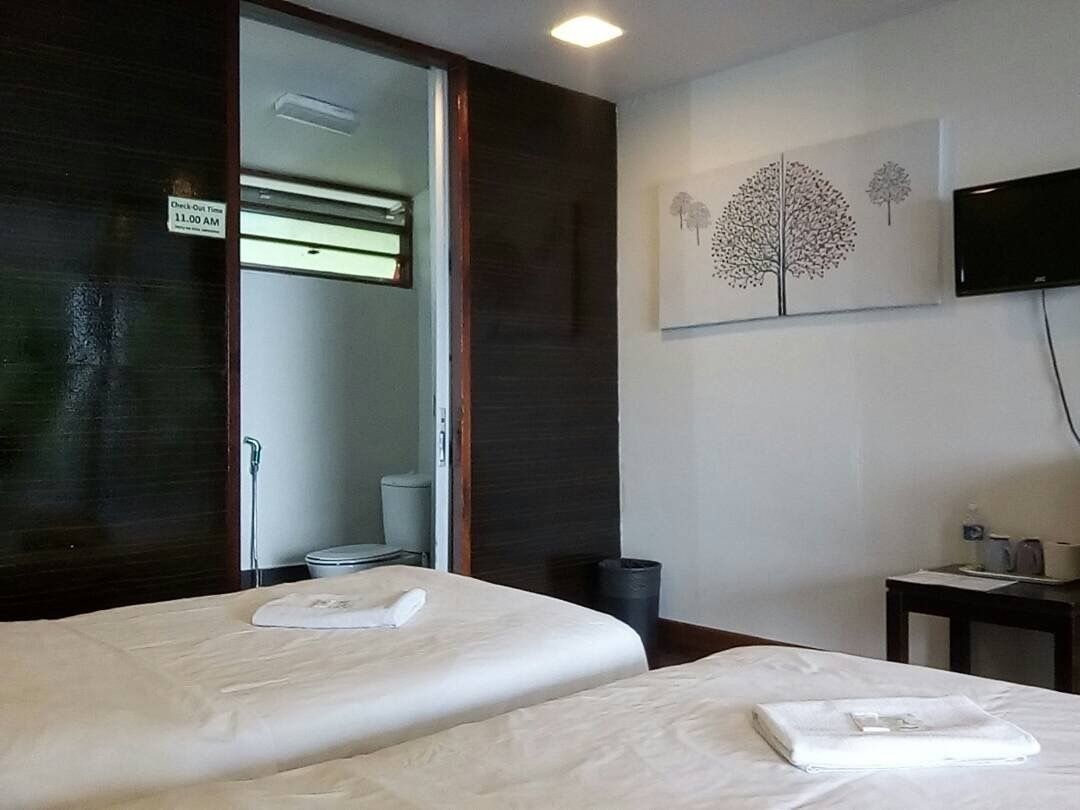 Ein Hotelzimmer mit zwei Betten, einem Badezimmer inklusive Toilette und Waschbecken, einem an der Wand befestigten Fernseher und einem Baumgemälde.