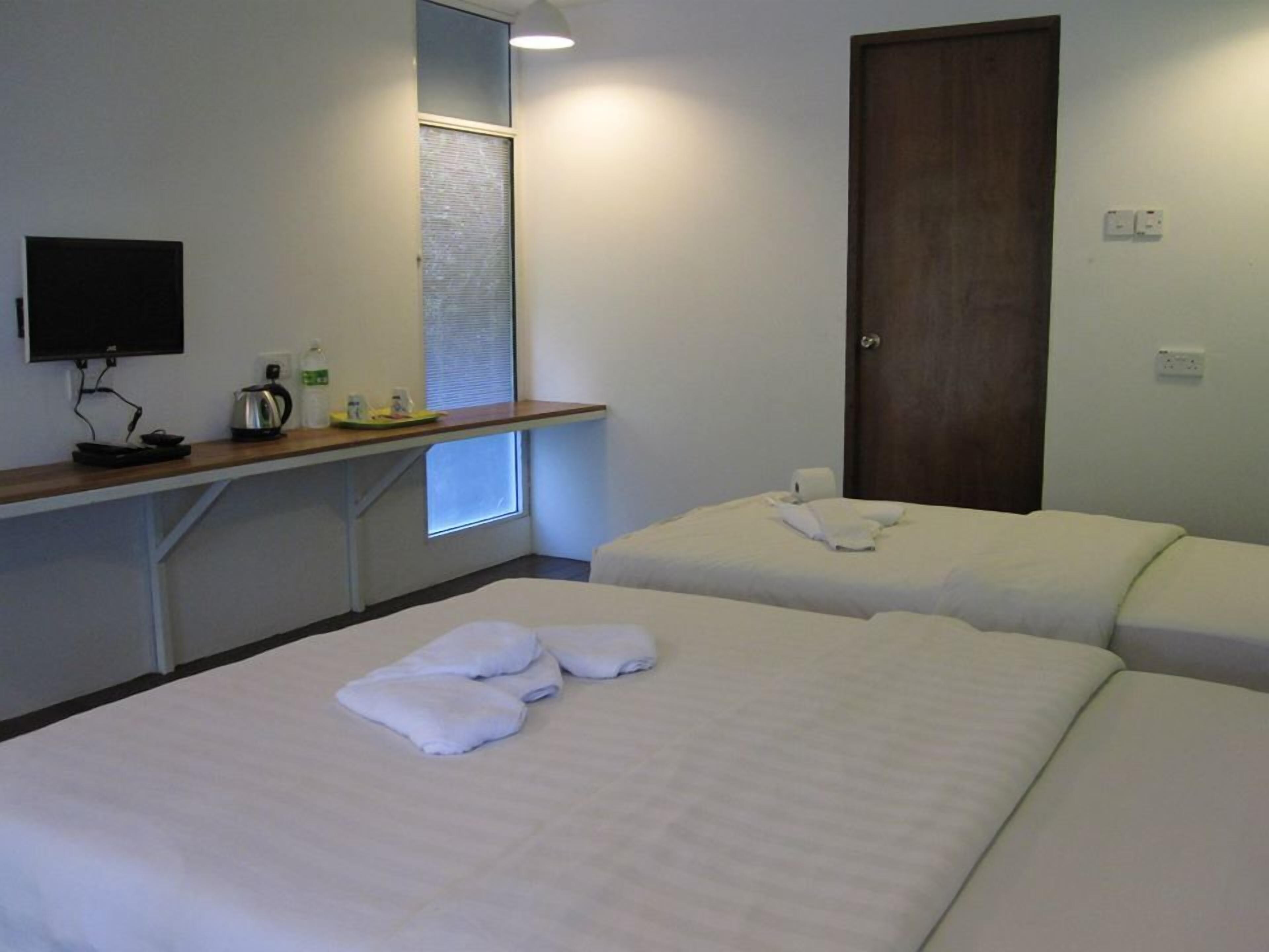 A hotel room with two beds, a small desk with a kettle, a TV, and a window with blinds.