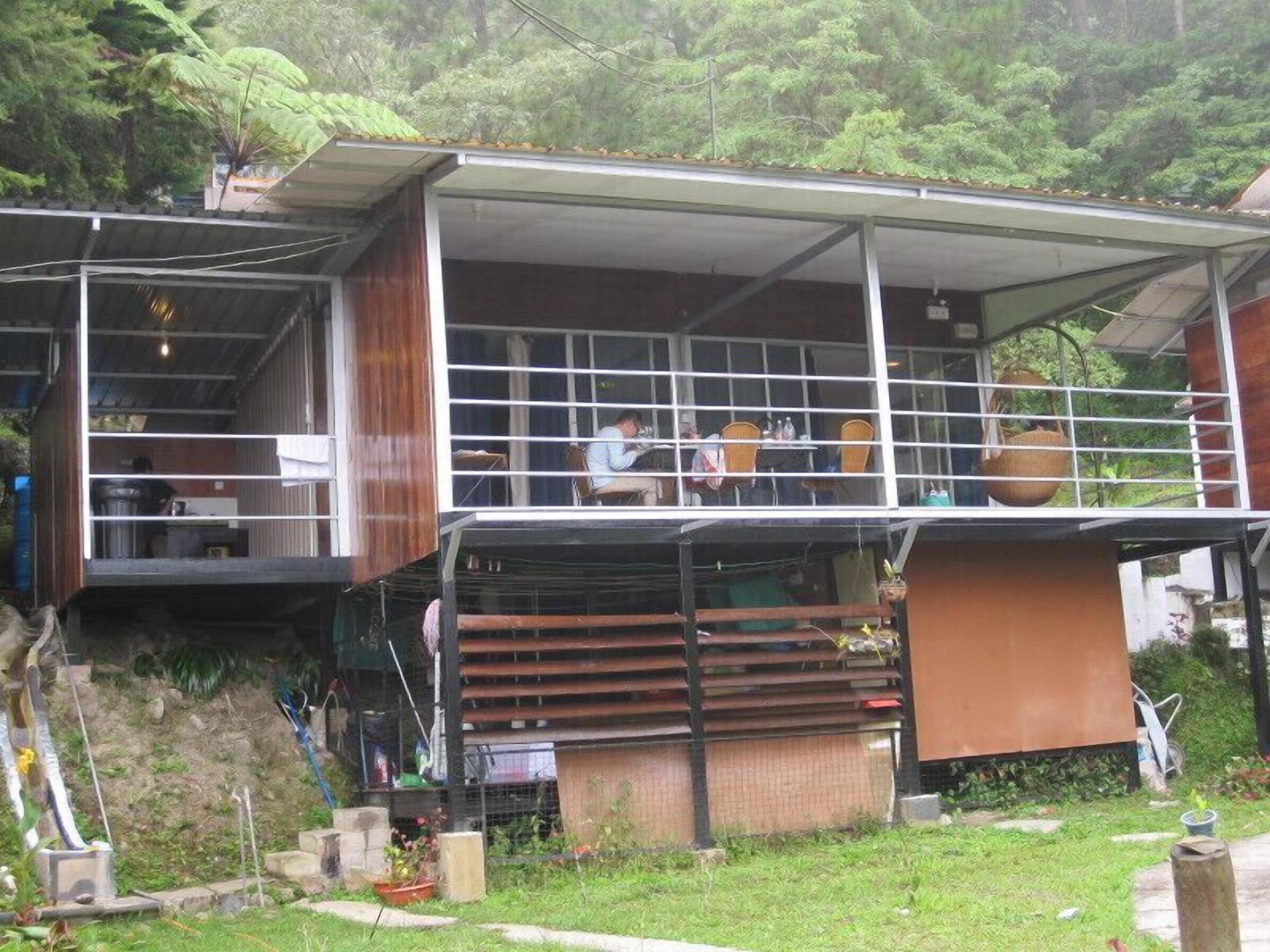 A two-story building with a balcony on the upper floor, surrounded by greenery.
