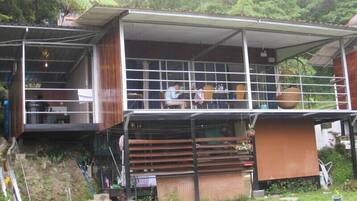 A two-story building with a balcony on the upper floor, surrounded by greenery.