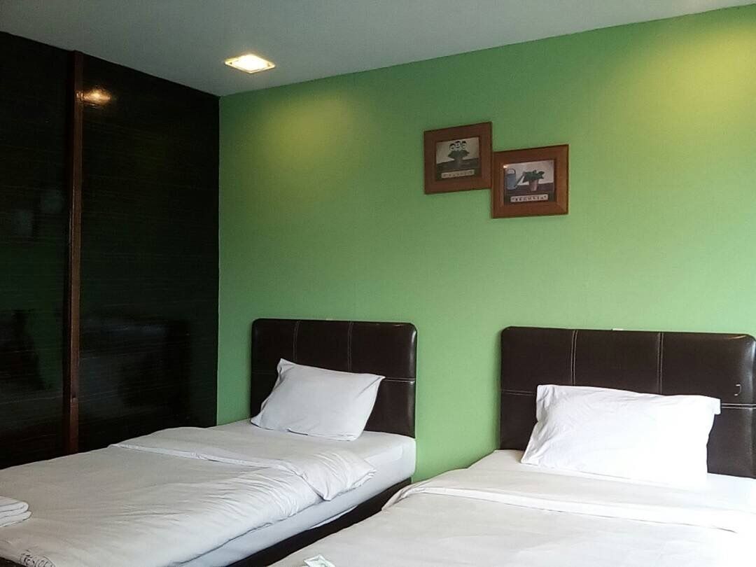 Habitación de hotel con dos camas, paredes verdes y cuadros en la pared.