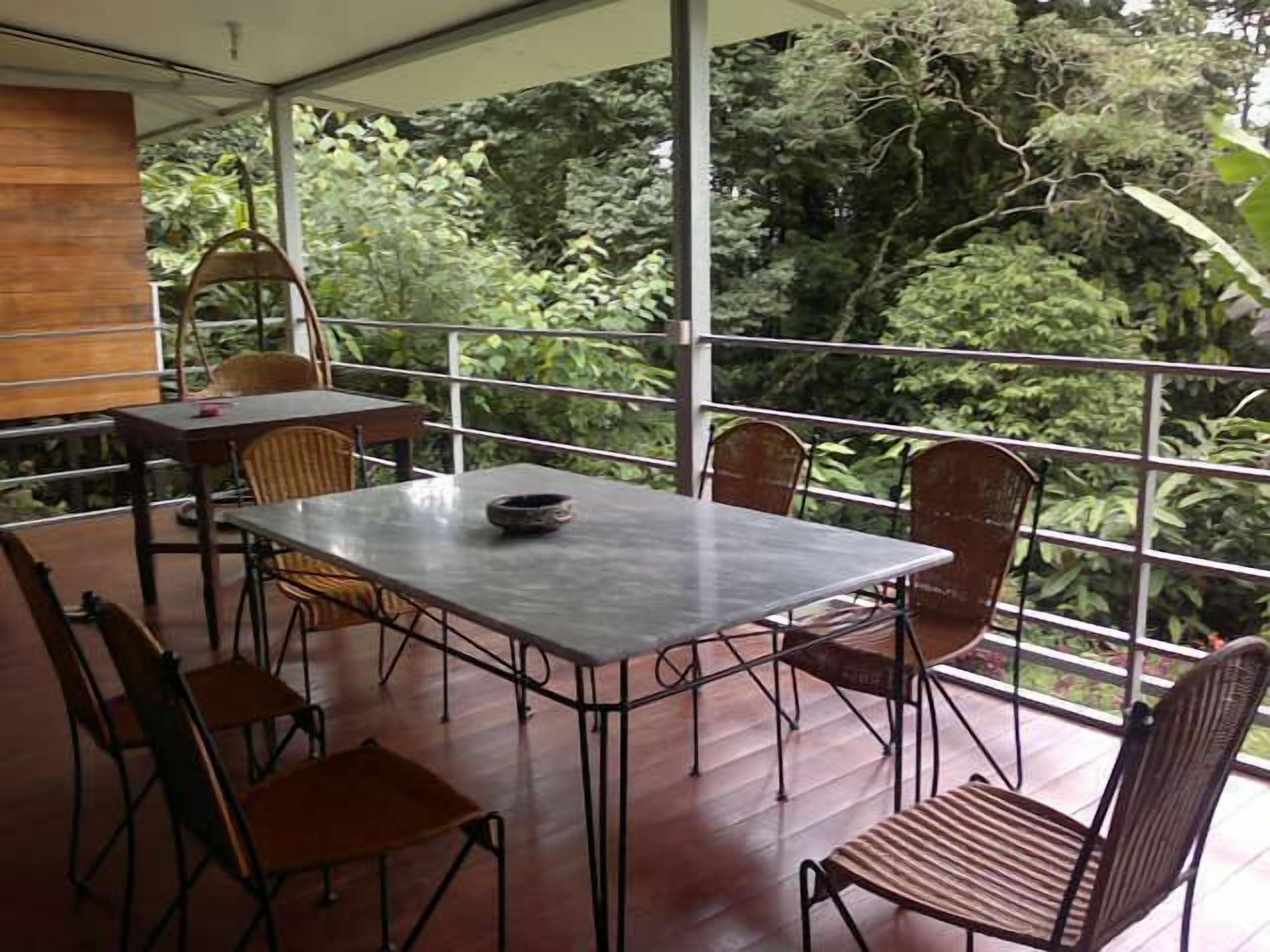 An outdoor dining area with a table and chairs, surrounded by a metal railing, overlooking a lush green landscape.