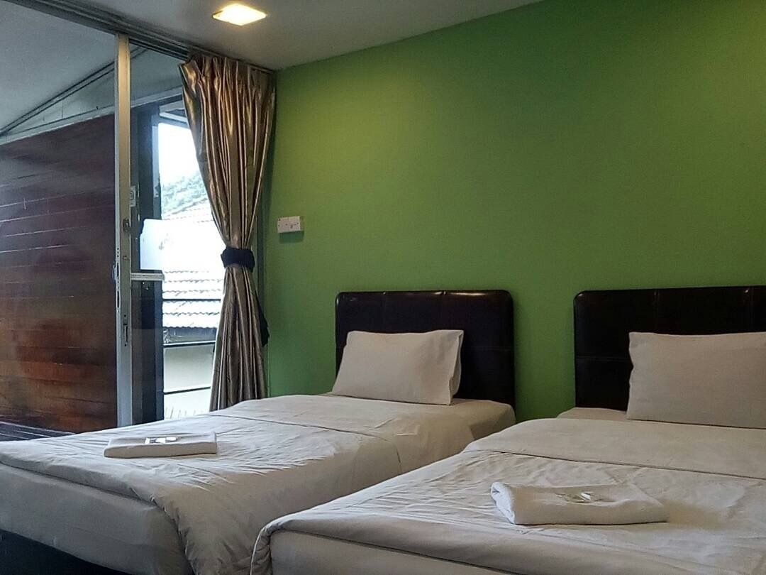 Habitación con dos camas, paredes verdes y una ventana con cortinas.