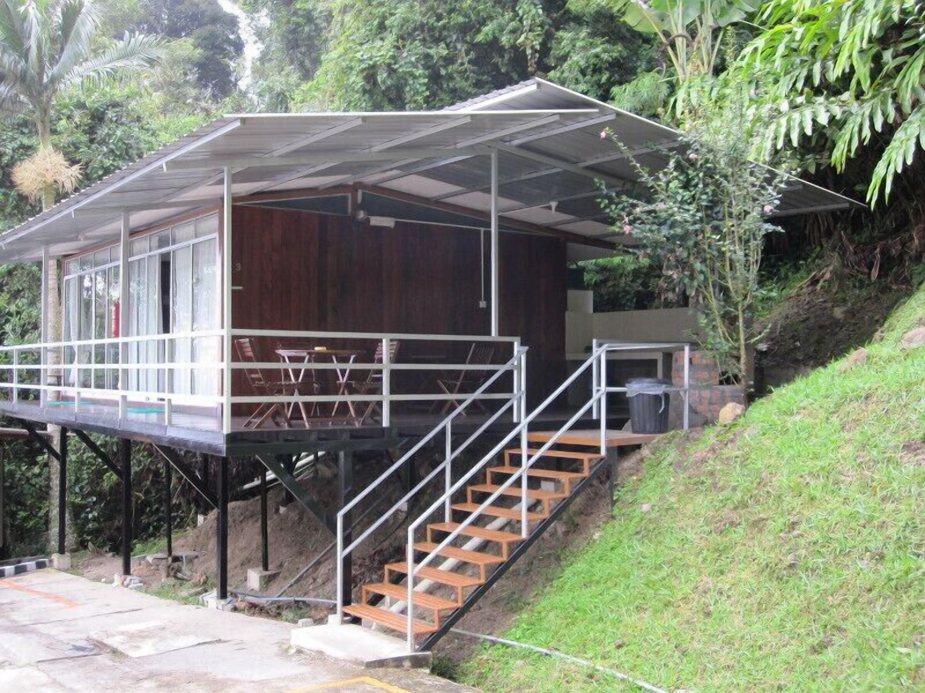A wooden cabin with a covered deck and stairs leading up to it, surrounded by greenery.