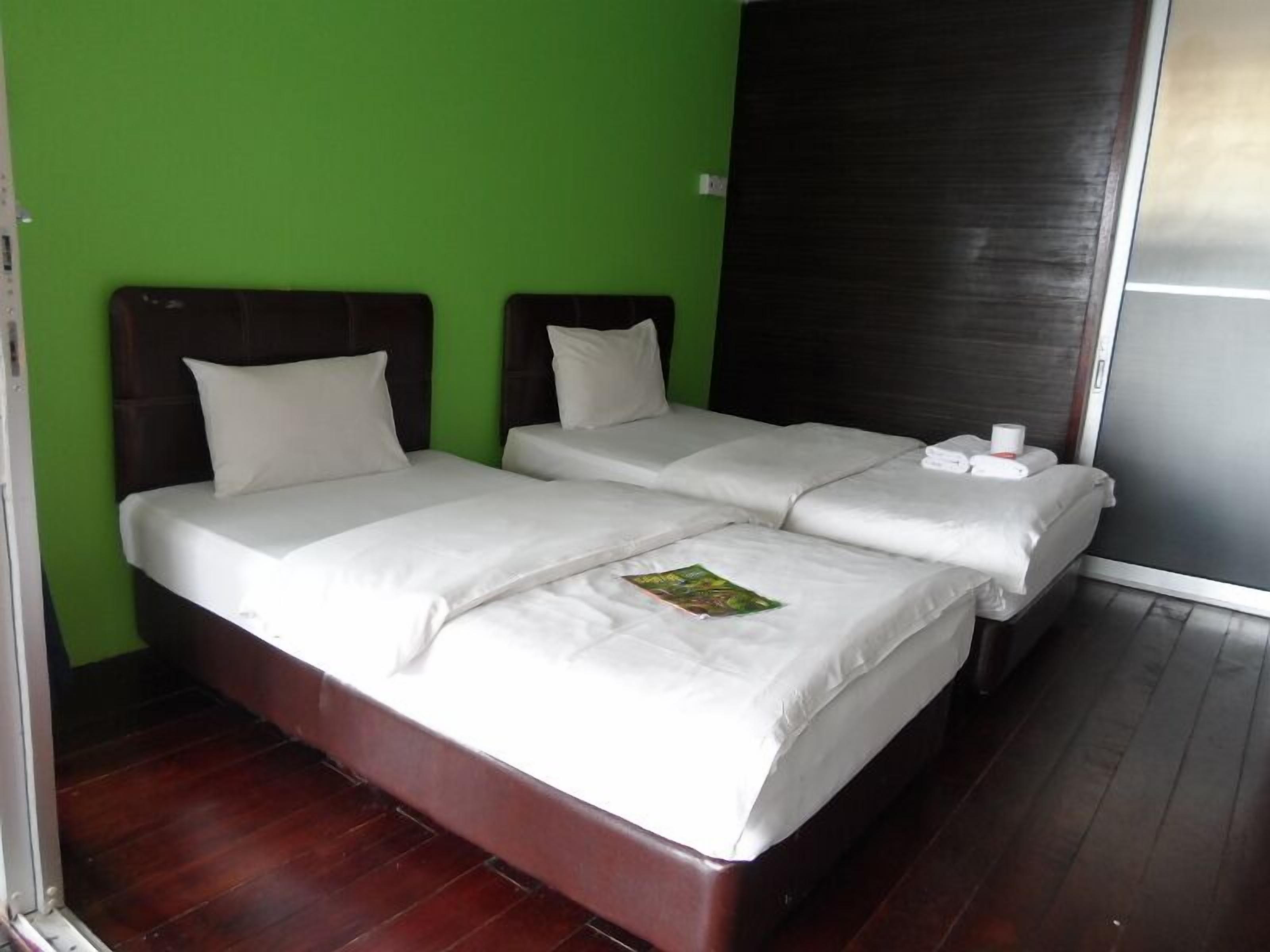 Een tweepersoonsbed met witte lakens, een groene wand en een donker houten hoofdeinde.