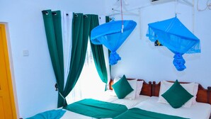 A room with two beds, green curtains, and mosquito nets.