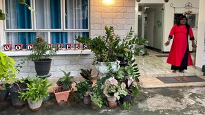 A hotel entrance with a stone facade, a 'GODESS' sign above the windows, and a variety of potted plants in front.
