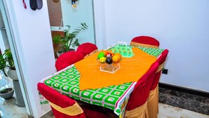 A dining table with a colorful tablecloth, red chairs, and a fruit bowl centerpiece.