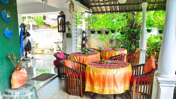 A covered outdoor seating area with tables and chairs, surrounded by greenery and plants.
