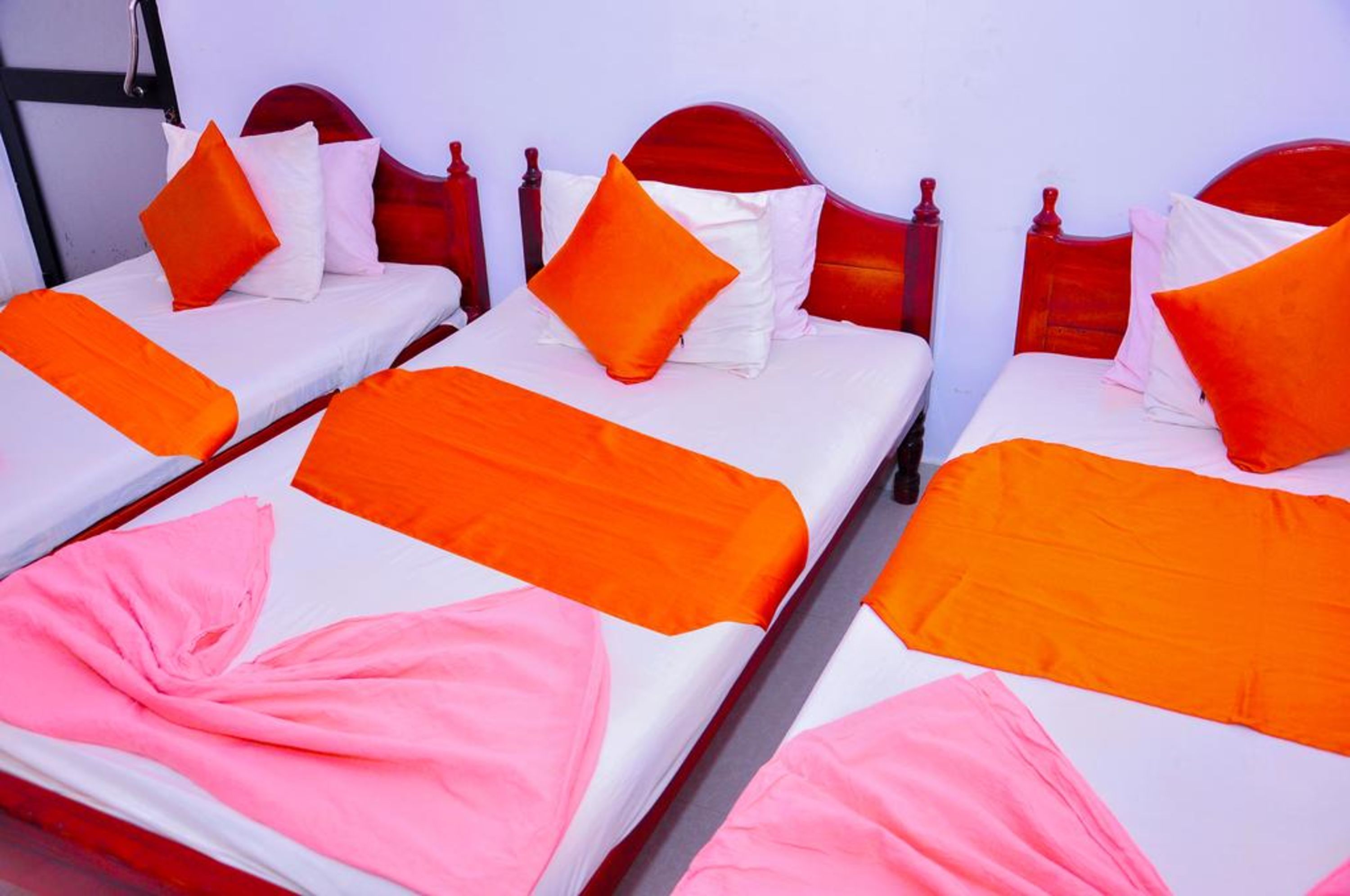 Three single beds with wooden headboards, white bedding, and orange and pink accents.