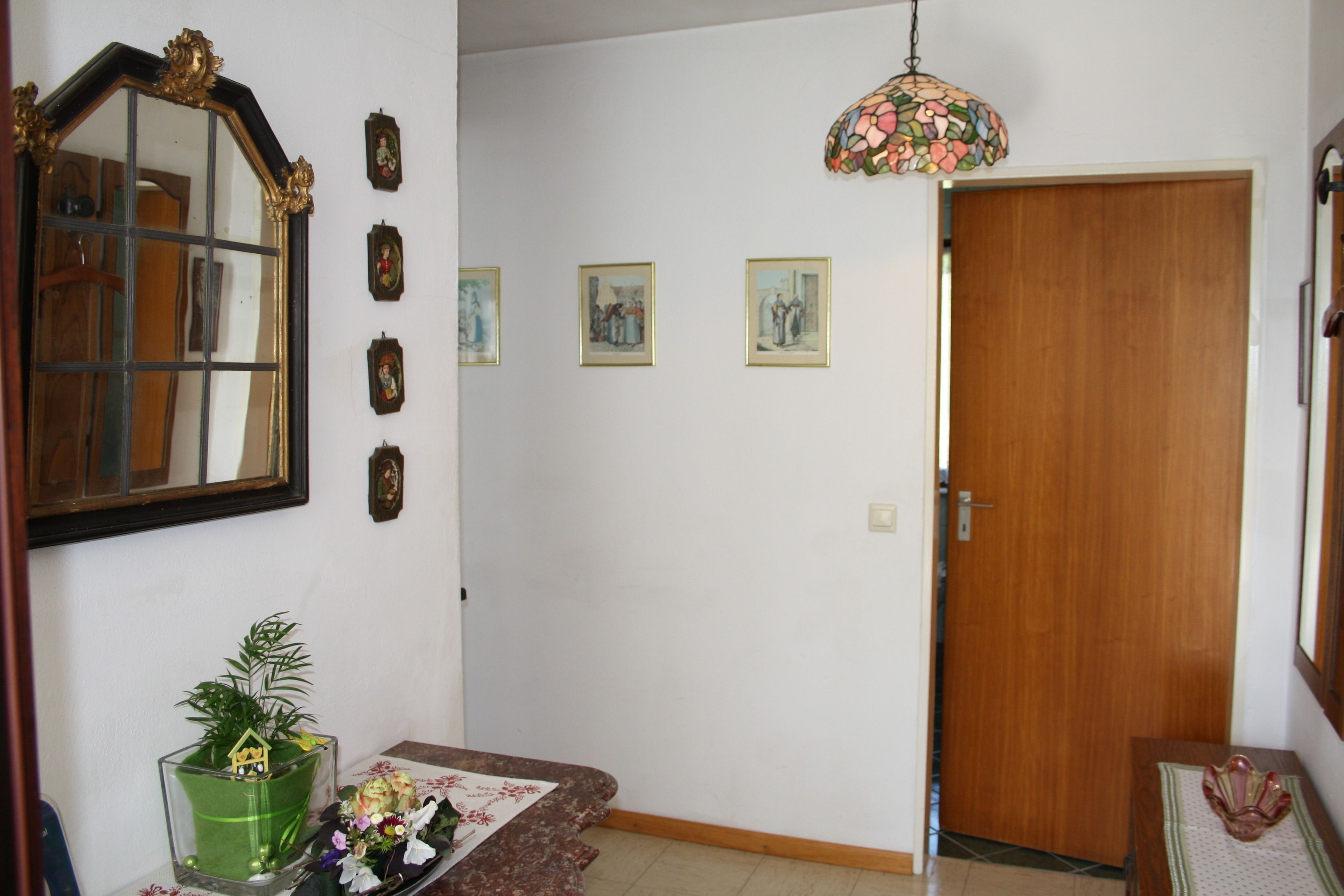 Un corridoio con una porta in legno, uno specchio e quadri appesi al muro.