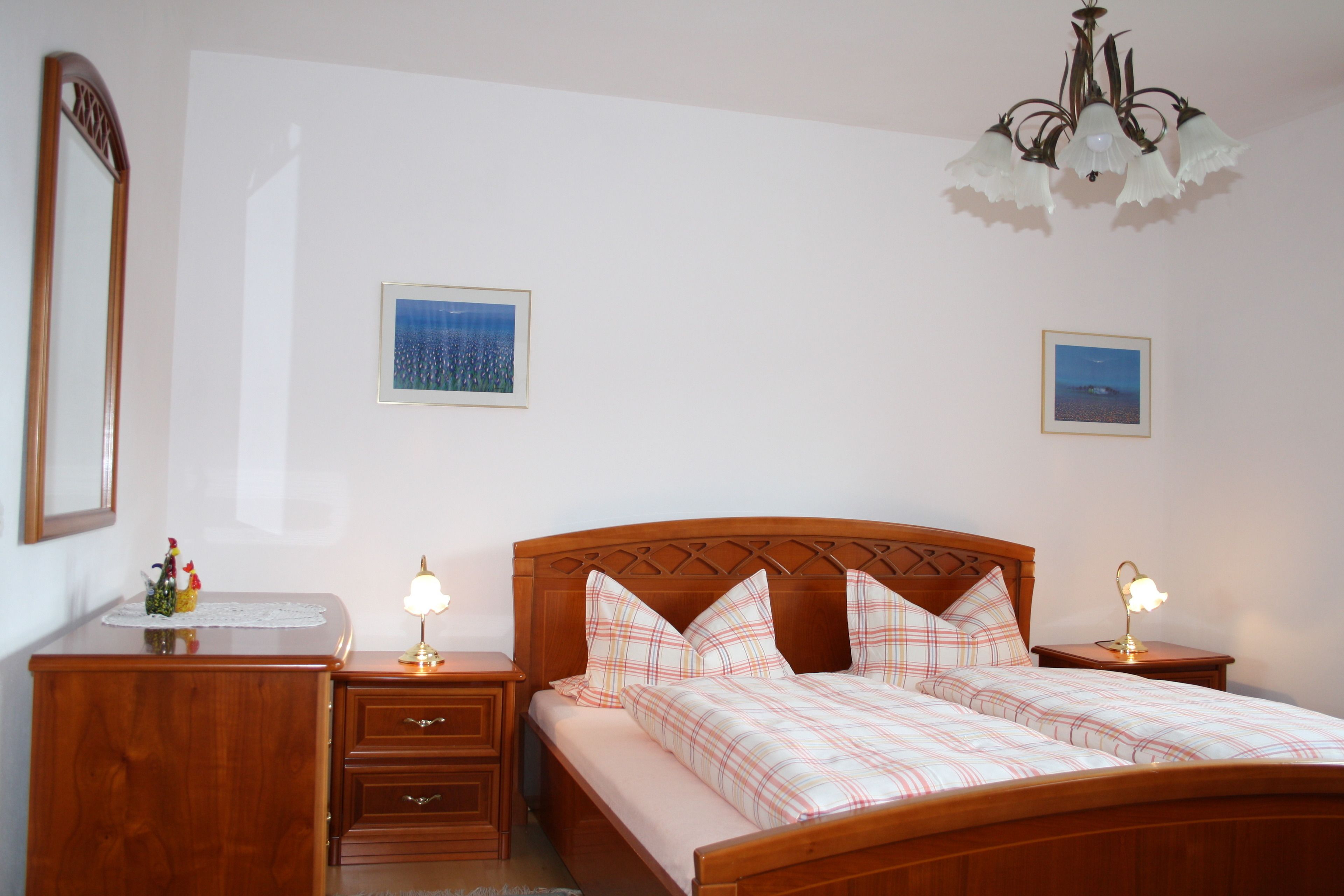 A bedroom with a wooden bed, bedside tables, a nightstand, and a chandelier.