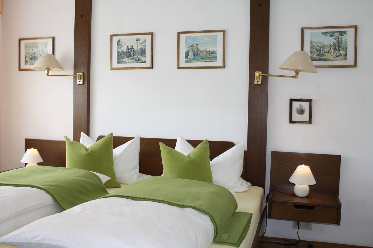Ein Hotelzimmer mit zwei Betten, Bettwäsche in Grün und Weiß sowie wandmontierten Lampen.