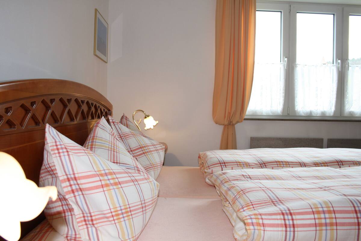 Ein Schlafzimmer mit zwei Betten, einem Holzkopfstück, einer Nachttischlampe und einem Fenster mit Vorhängen.