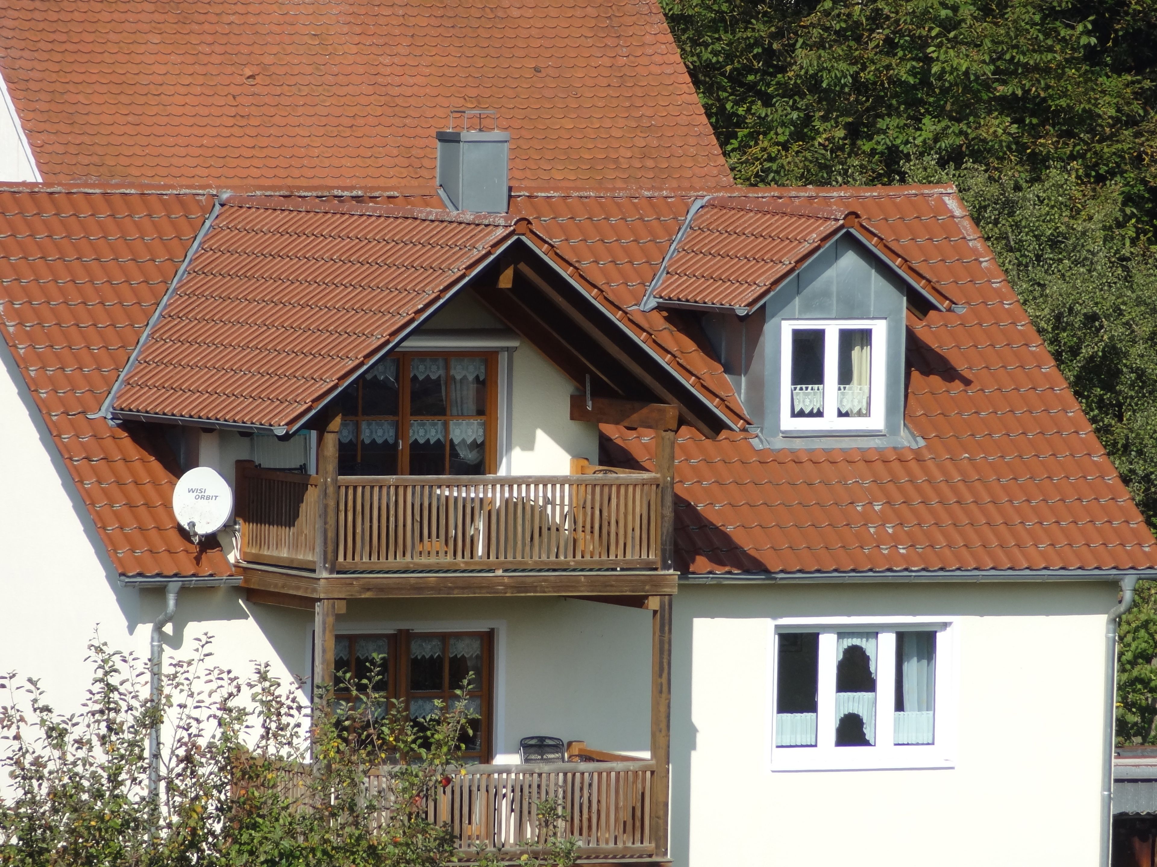A two-story house with a balcony, a satellite dish, and a small attic window.