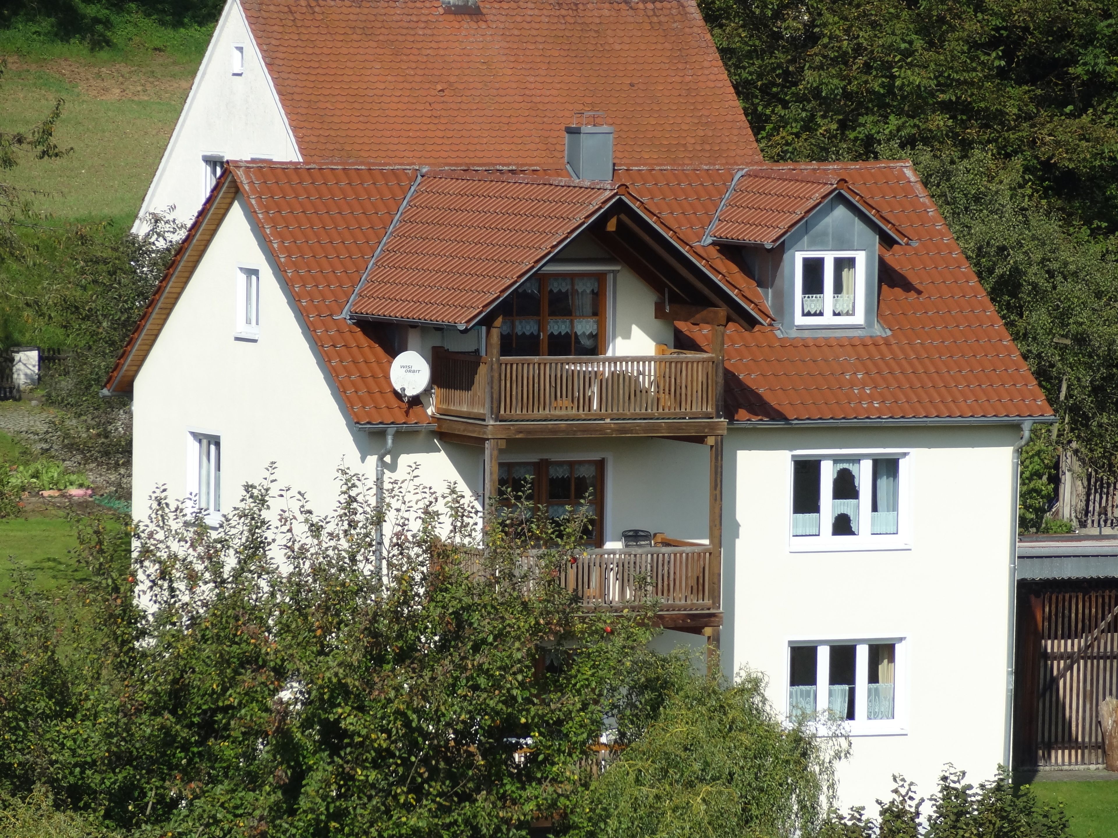 A two-story house with a brown tiled roof, a balcony, and a satellite dish.