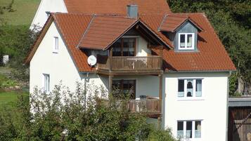 A two-story house with a brown tiled roof, a balcony, and a satellite dish.