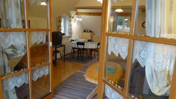 Una habitación acogedora con zona de comedor, televisión y ventana con cortinas de encaje.
