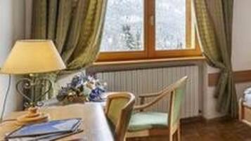 A bedroom with a bed, a chair, a desk with a lamp, and a window with curtains.