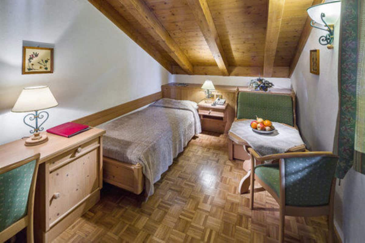 A cozy attic bedroom with two single beds, a small table with fruit, a chair, and a desk with a lamp.