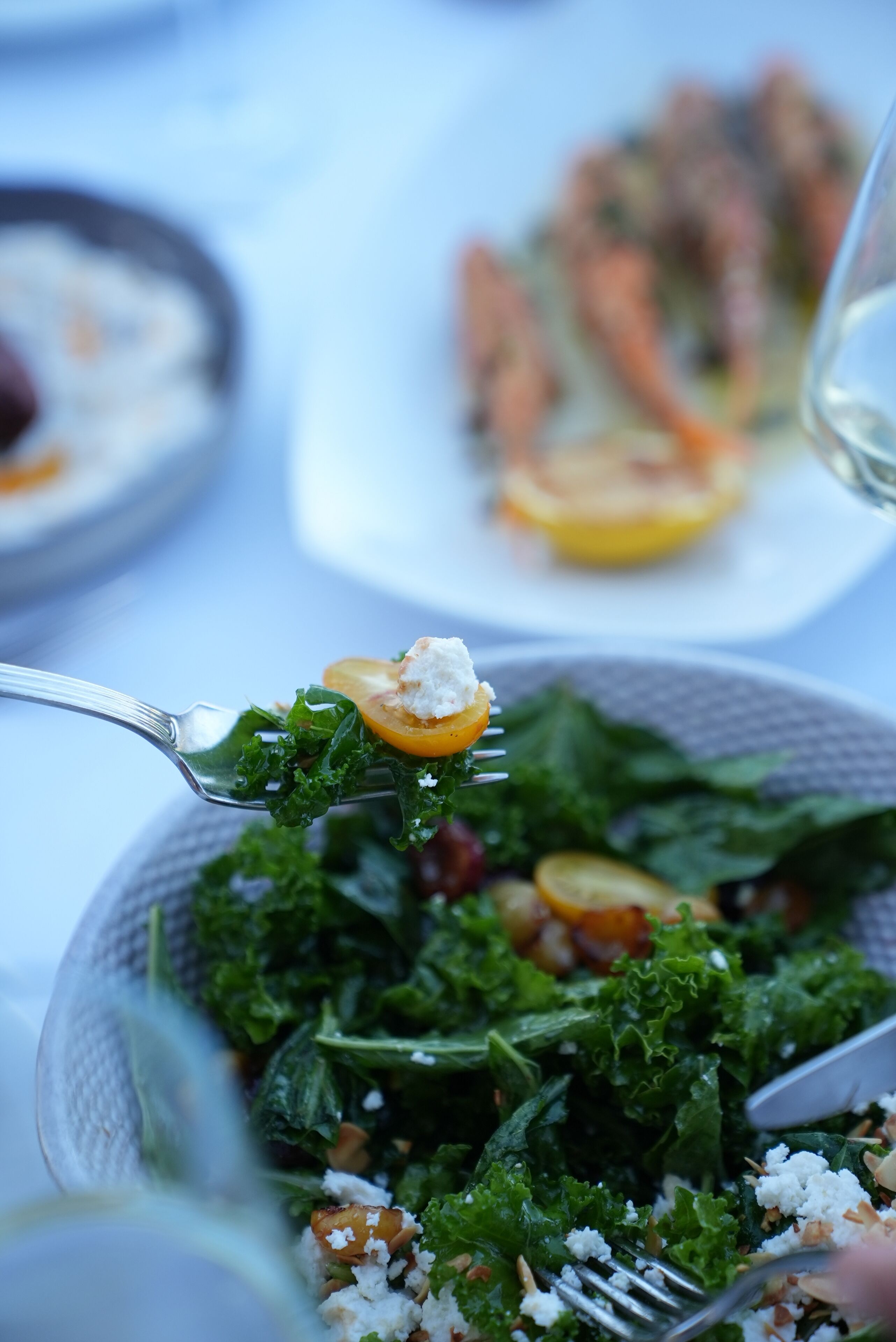 A close-up of a salad with a fork, and a blurred background of a dining table with plates.