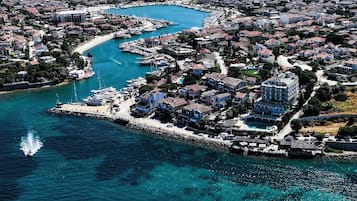 Vista aérea de un pueblo costero con un puerto deportivo, edificios residenciales y un mar azul y despejado.