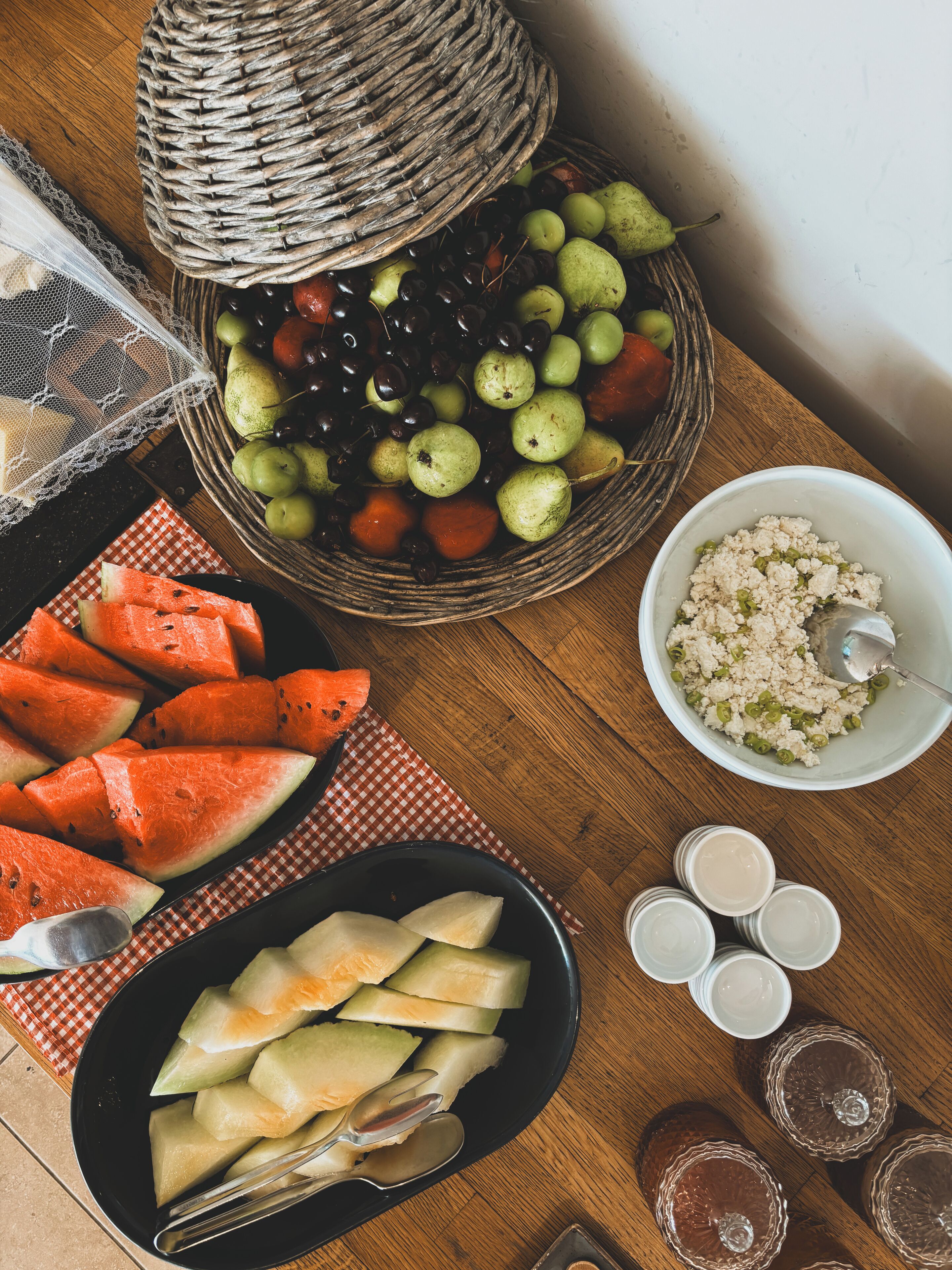 A wooden table with a fruit basket, watermelon slices, melon pieces, and a bowl of food.