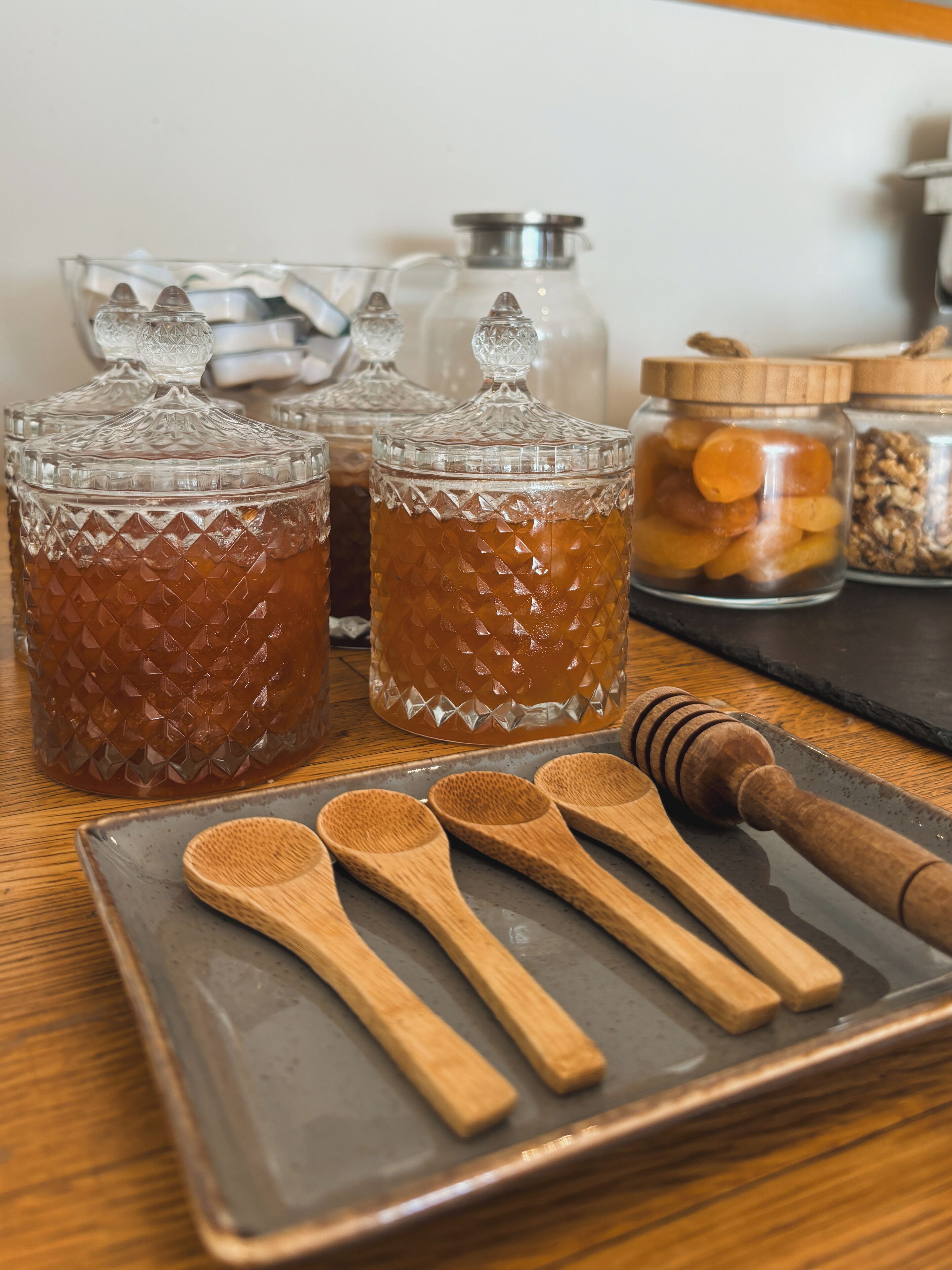 Three glass containers with textured surfaces, a wooden spoon set, and a honey dipper on a tray.