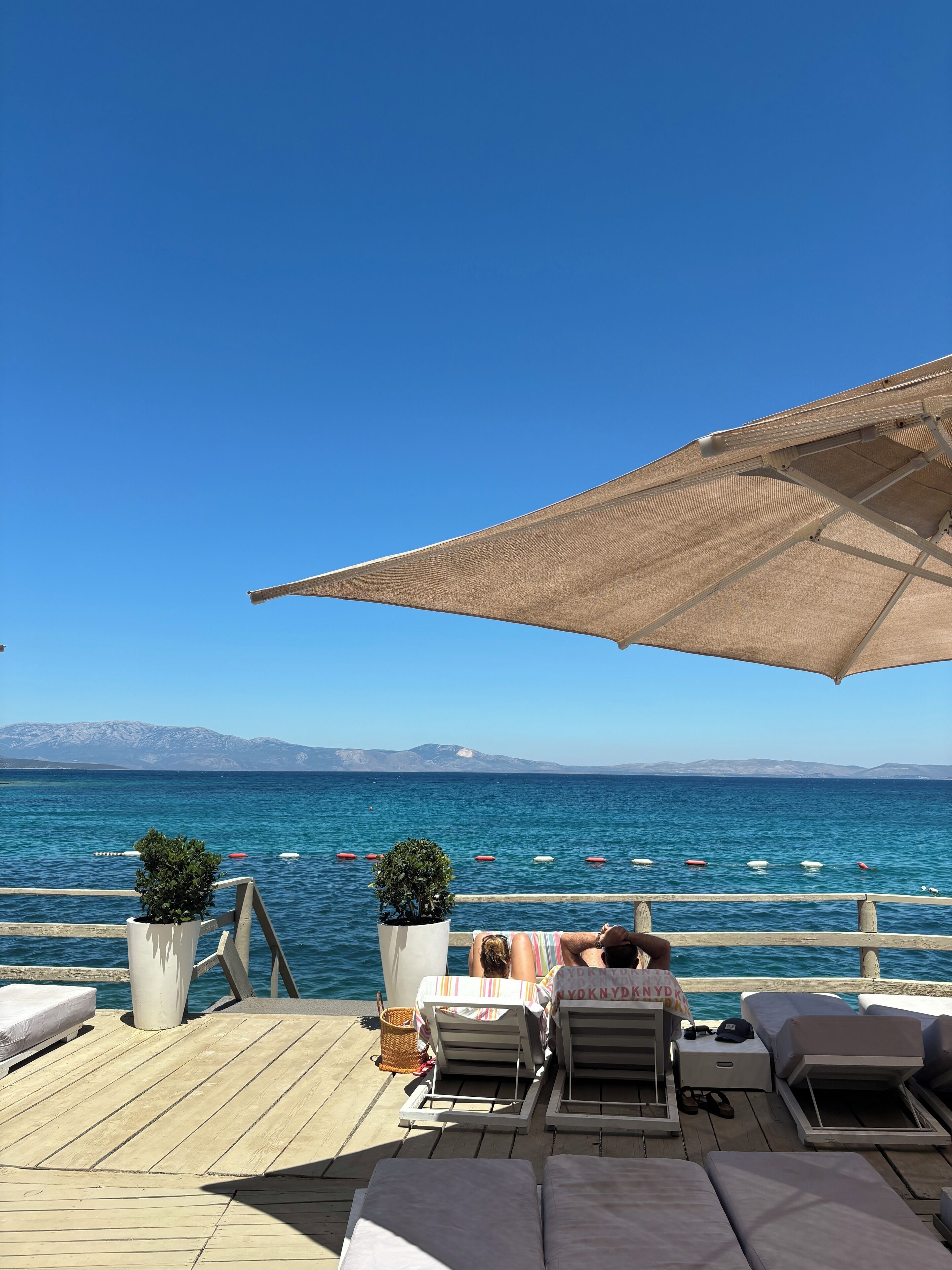 A deck with lounge chairs and umbrellas overlooking a calm sea with boats.