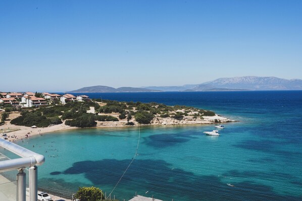 A coastal town with a beach, clear blue sea, and mountains in the background.