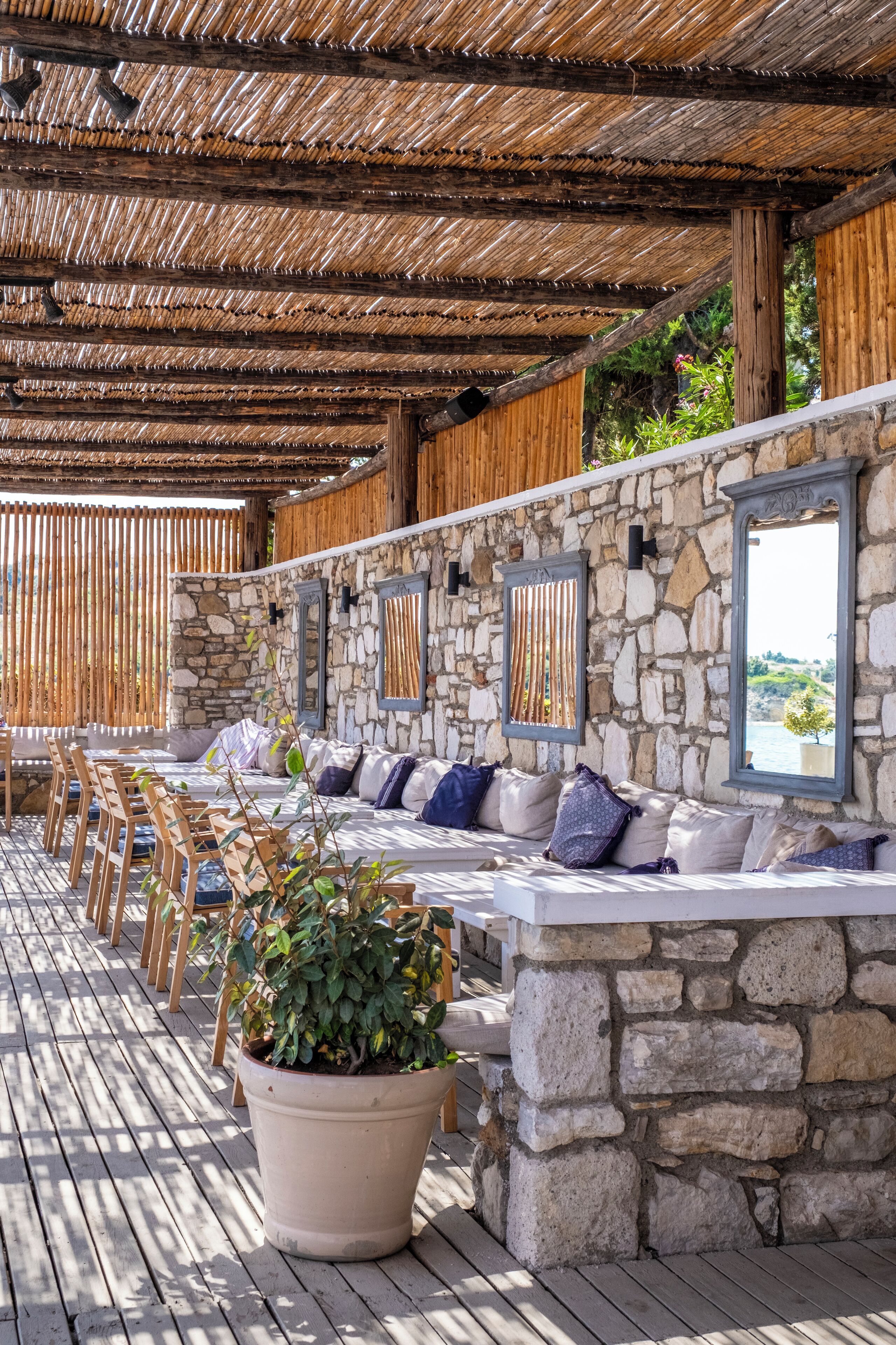 An outdoor seating area with stone walls, wooden chairs, and a large potted plant.