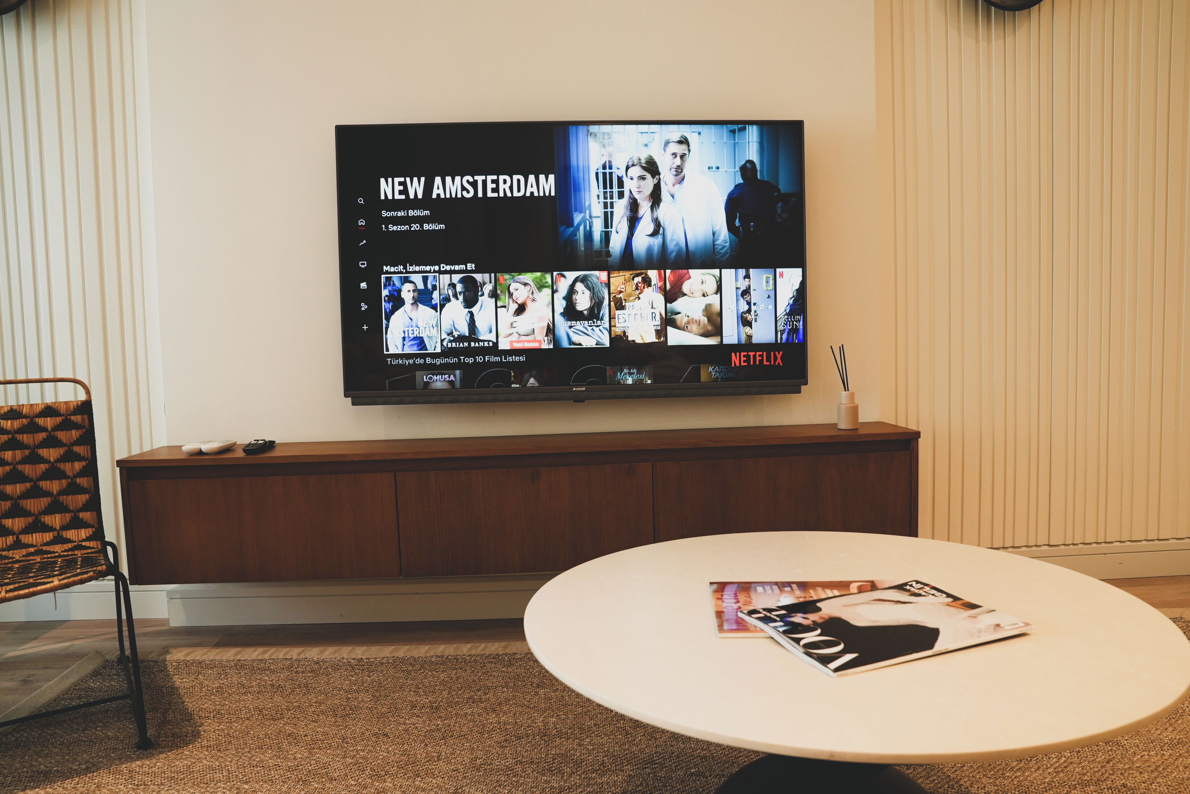 Una sala de estar moderna con un televisor de pantalla plana mostrando la interfaz de Netflix, una mesa de centro redonda con revistas y un mueble bajo de madera.