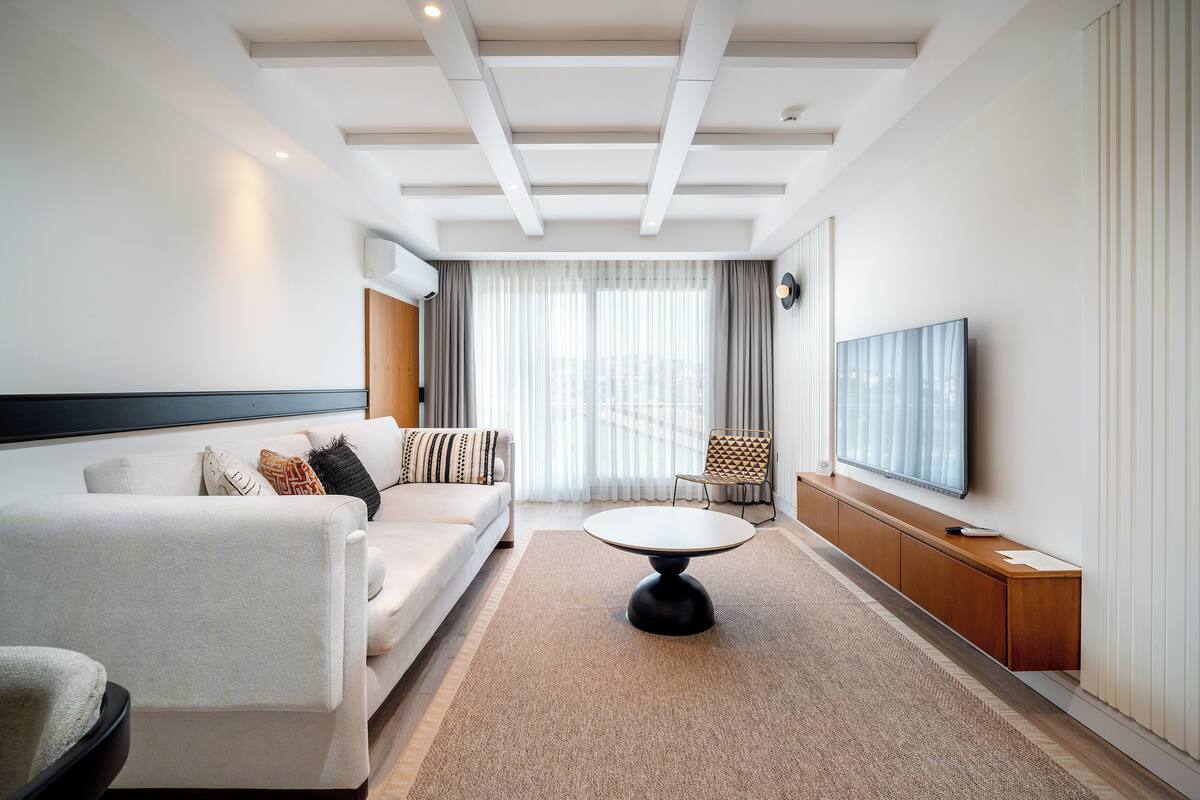 A modern living room with a sofa, a coffee table, a TV, and a view of the city through large windows.