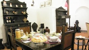 A dining area with a wooden table set for four, surrounded by chairs. There are various dishes and condiments on the table, and a decorative shelf with kitchenware above it. - B&B Il Glicine Residenza D'Epoca (Torrita di Siena)