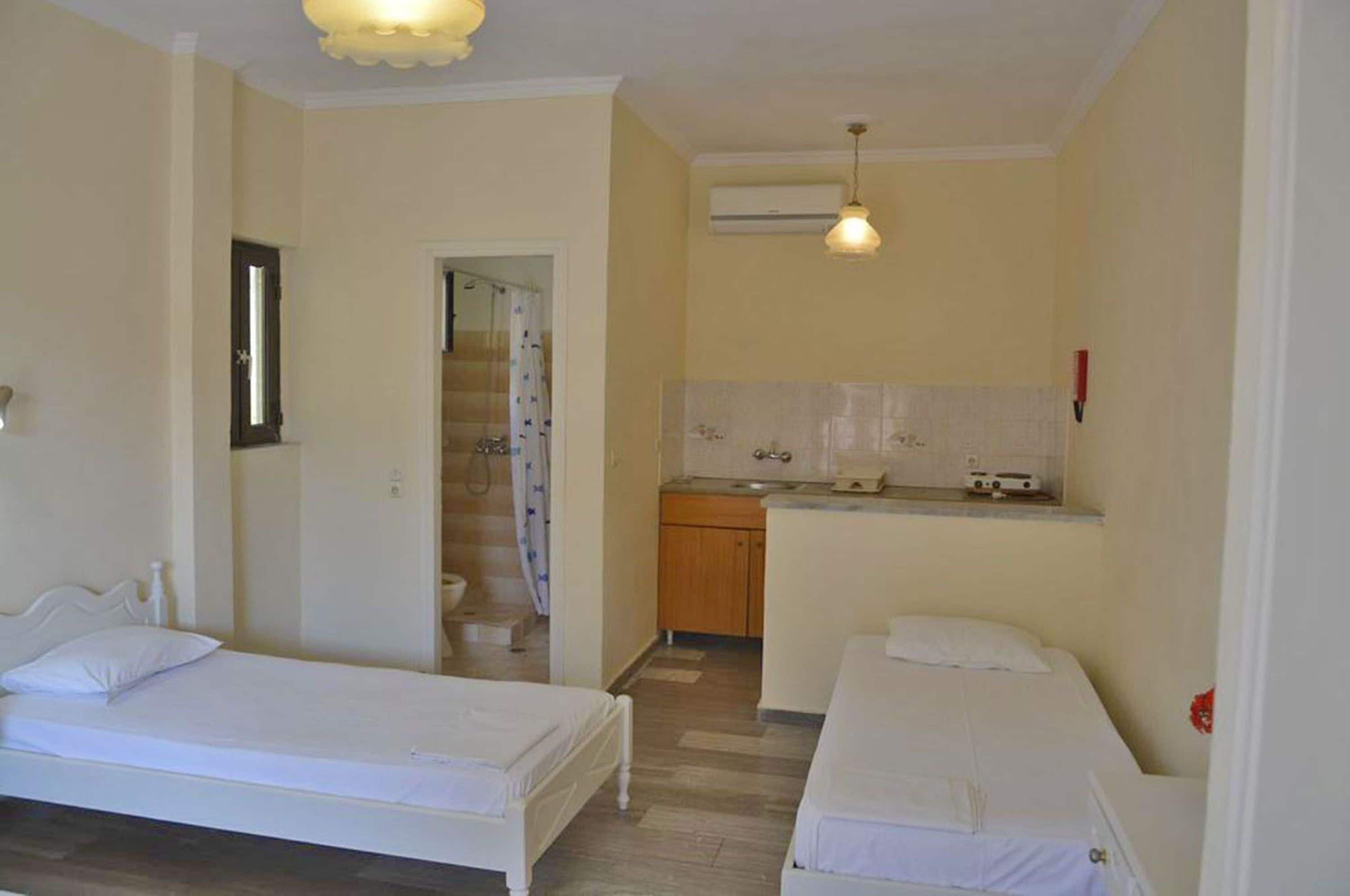 A small, clean room with two single beds, a kitchenette, and a shower area.