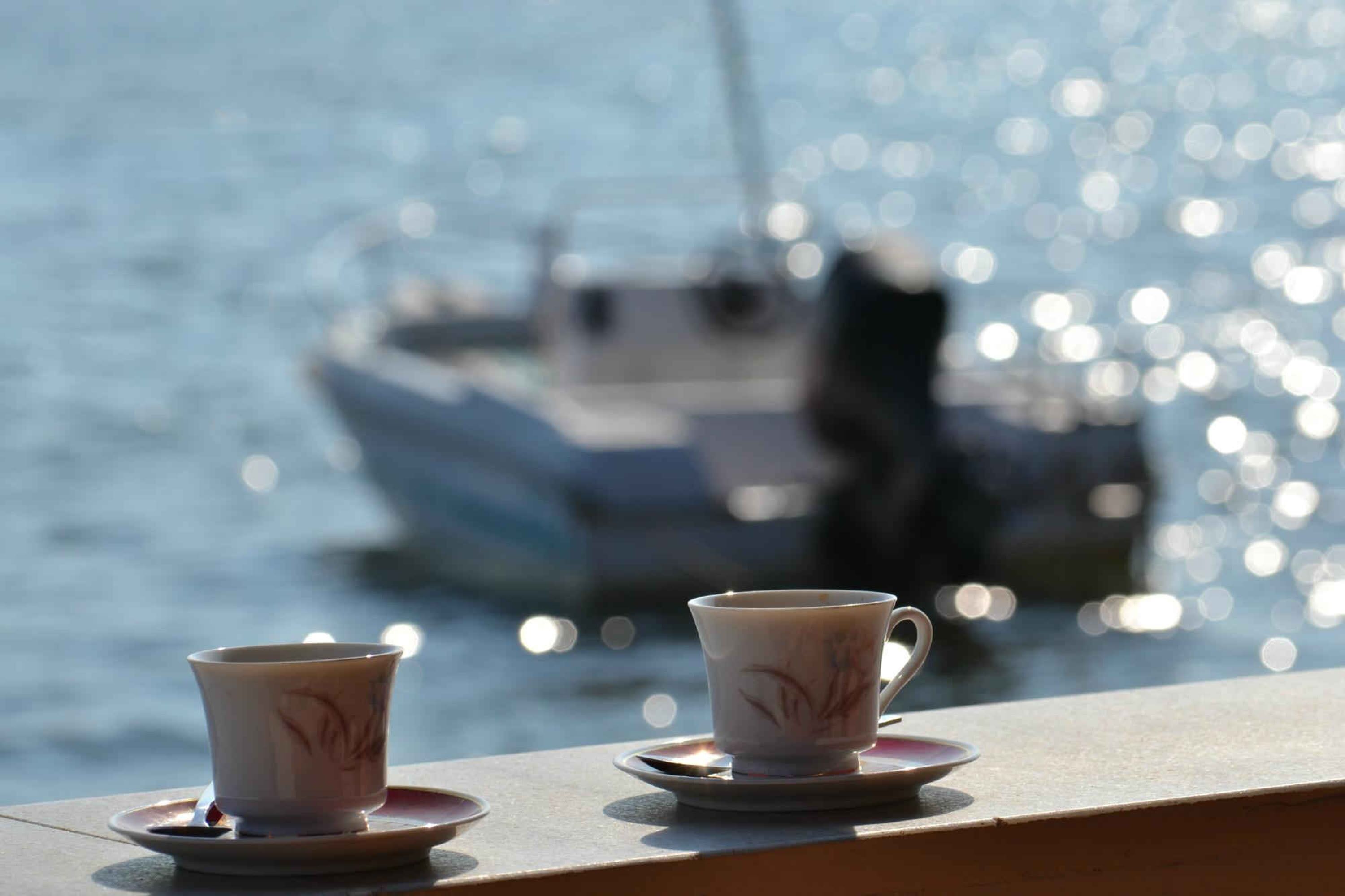 Two cups on a table with a view of a boat in the background.