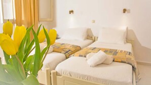 Une chambre d’hôtel avec deux lits, un vase de tulipes jaunes et une fenêtre avec des rideaux.
