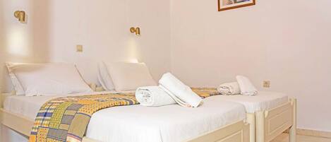 A hotel room with two beds, a patterned blanket, and a painting on the wall.