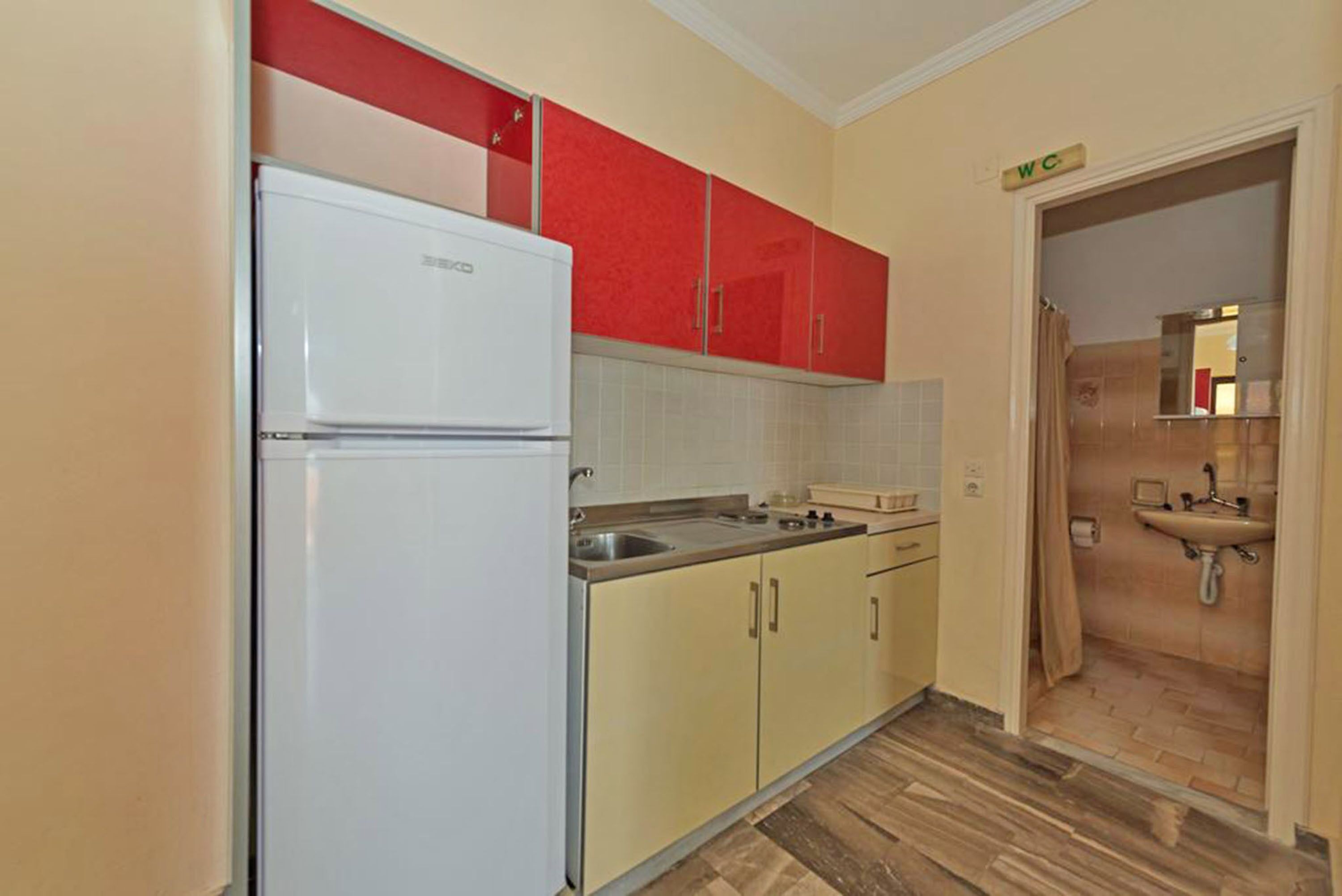 Une cuisine de taille réduite avec un réfrigérateur blanc, des placards de couleur beige et une partie supérieure rouge.