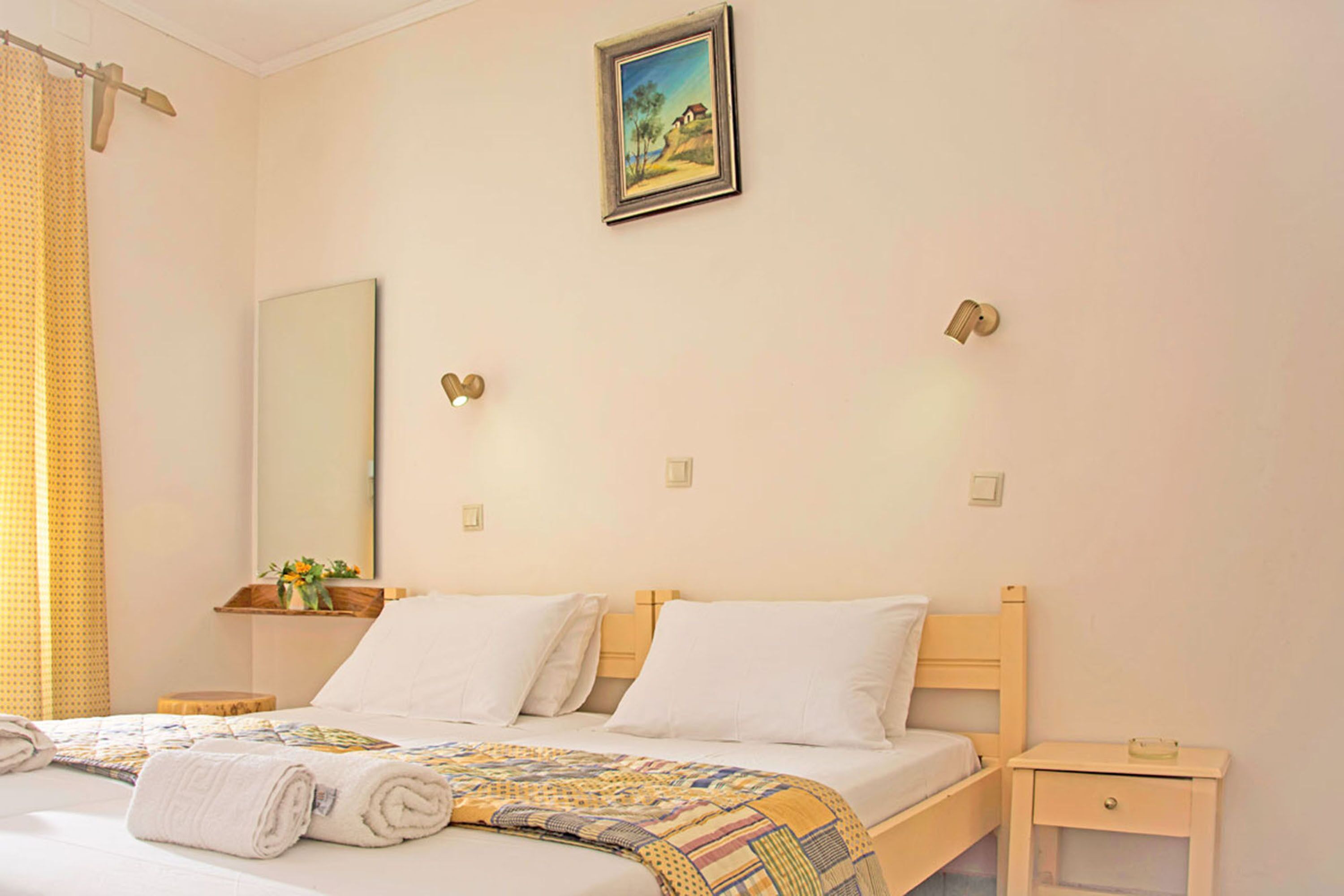 A bedroom with a bed, a nightstand, a bedside table, a mirror, and a painting on the wall.