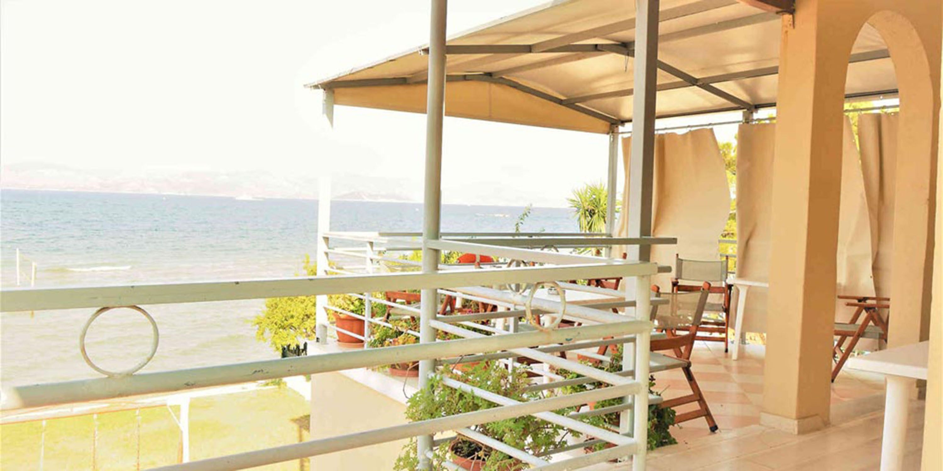 A balcony with a view of the sea, a covered seating area, and potted plants.