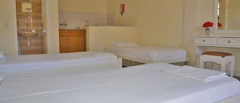 Habitación de hotel con dos camas individuales, baño pequeño con lavamanos y tocador con espejo.