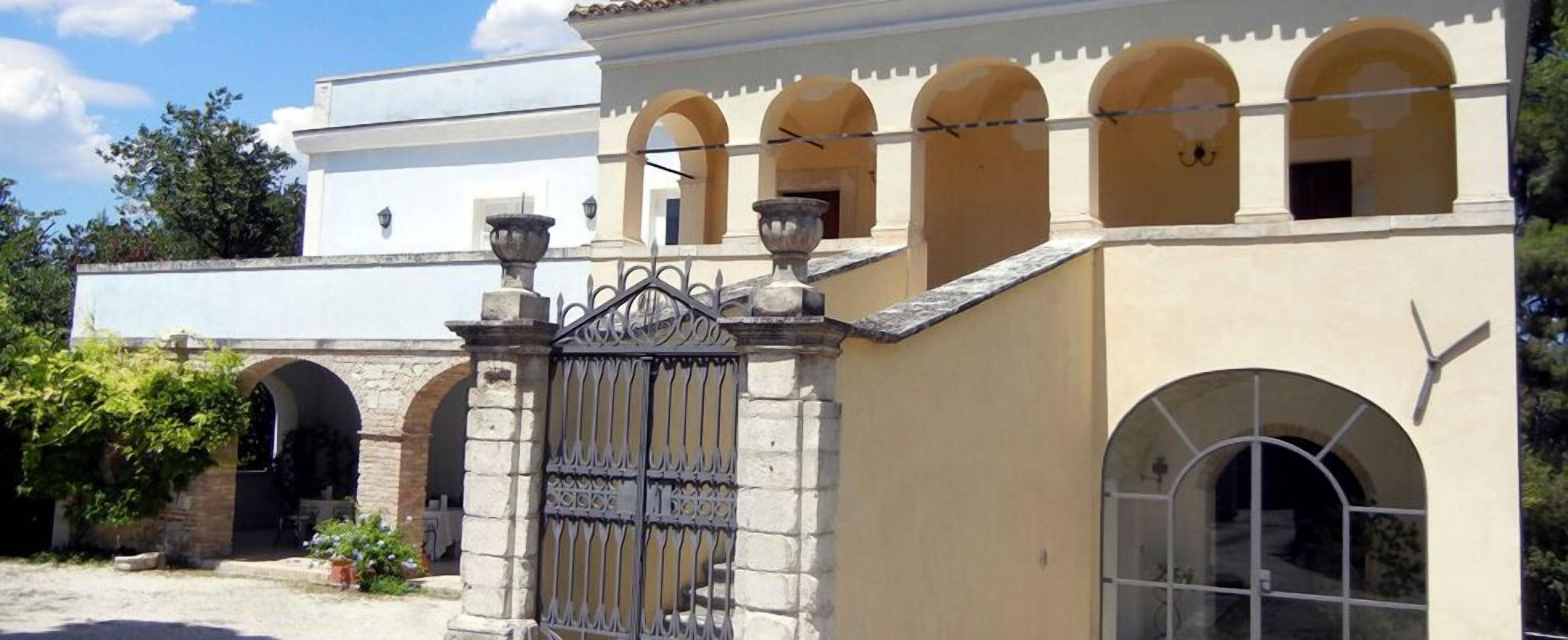 Un bâtiment à la façade beige, doté de fenêtres en arc de cercle et d’une grille en métal décorative.