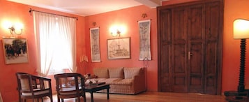 Una habitación con sofá, sillas, una mesa, una puerta de madera y luces fijadas en la pared.