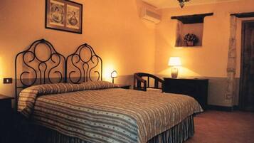 A bedroom with a bed, a nightstand, a chair, a lamp, and a wall-mounted shelf with a plant.
