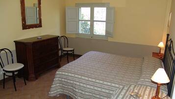Un dormitorio con cama, cómoda, silla y ventana con contraventanas.