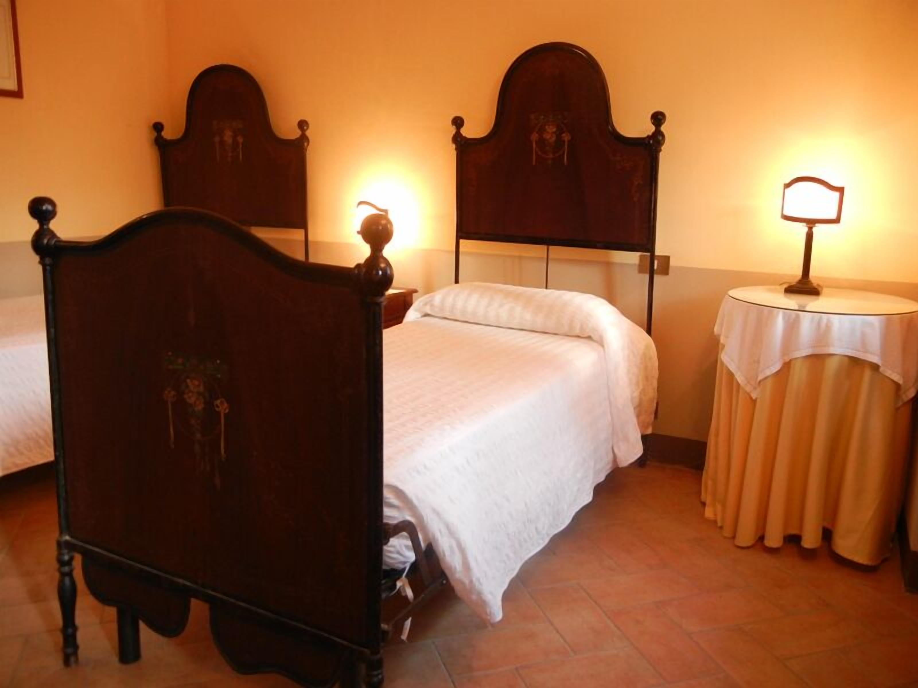 Une chambre d’hôtel avec deux lits, une table ronde avec une lampe et un miroir au mur.