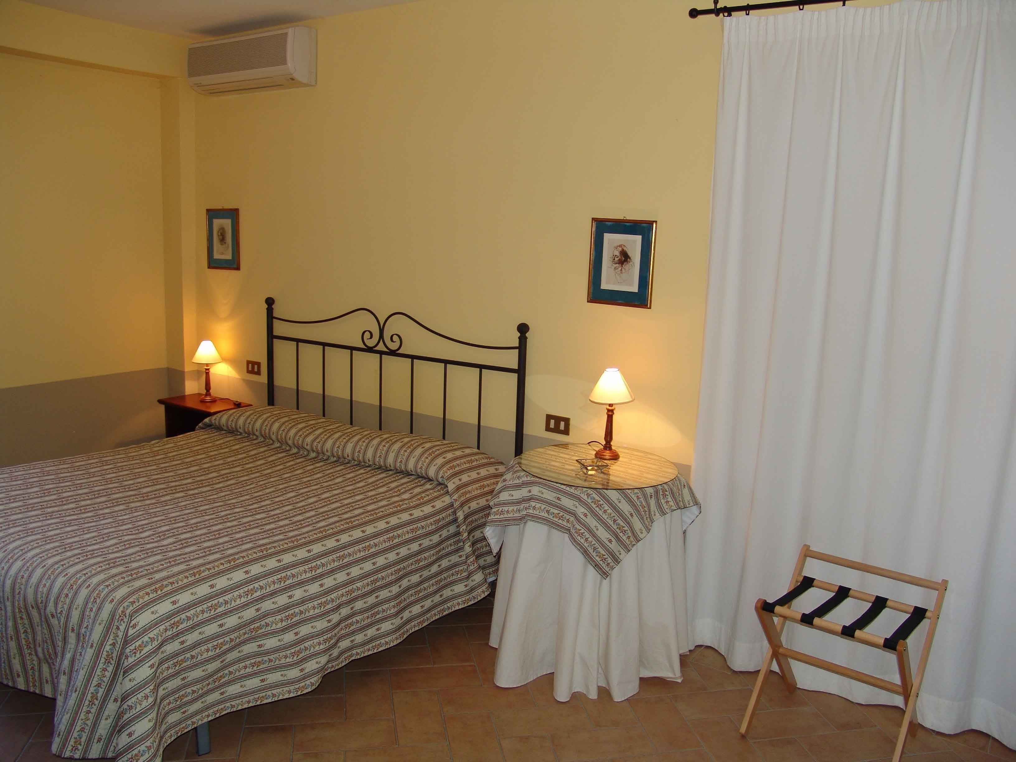 A bedroom with two beds, a bedside table with a lamp, a chair, and a curtain.