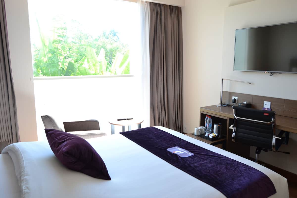 Habitación de hotel con cama, escritorio, silla, televisor y ventana con cortinas.